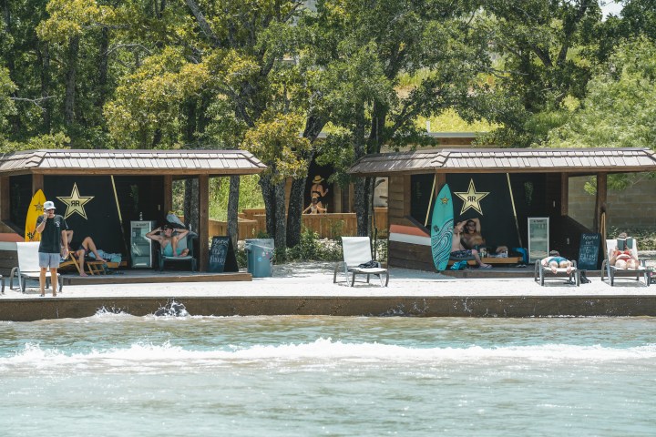 Guests lounging in Waco Surf's beach cabanas, watching the surf lagoon