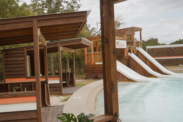 Wooden cabanas overlooking a pool with water slides in an outdoor setting.