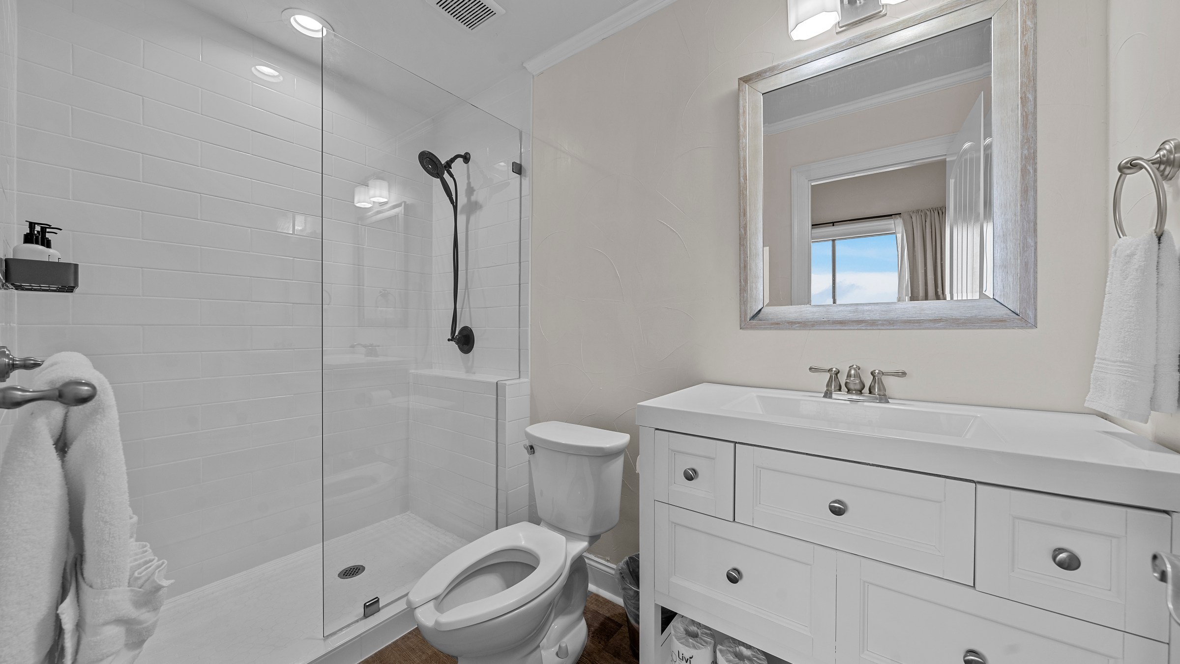 Modern bathroom with glass shower, white vanity, and large mirror reflecting window view.