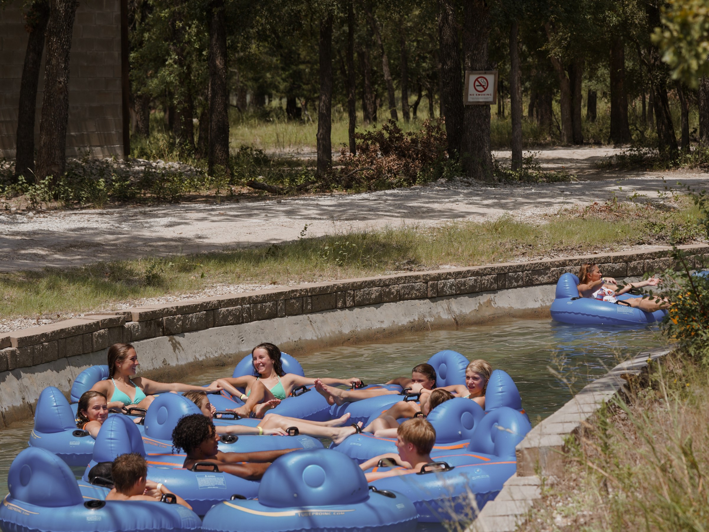 People floating in blue inner tubes on a lazy river surrounded by trees.