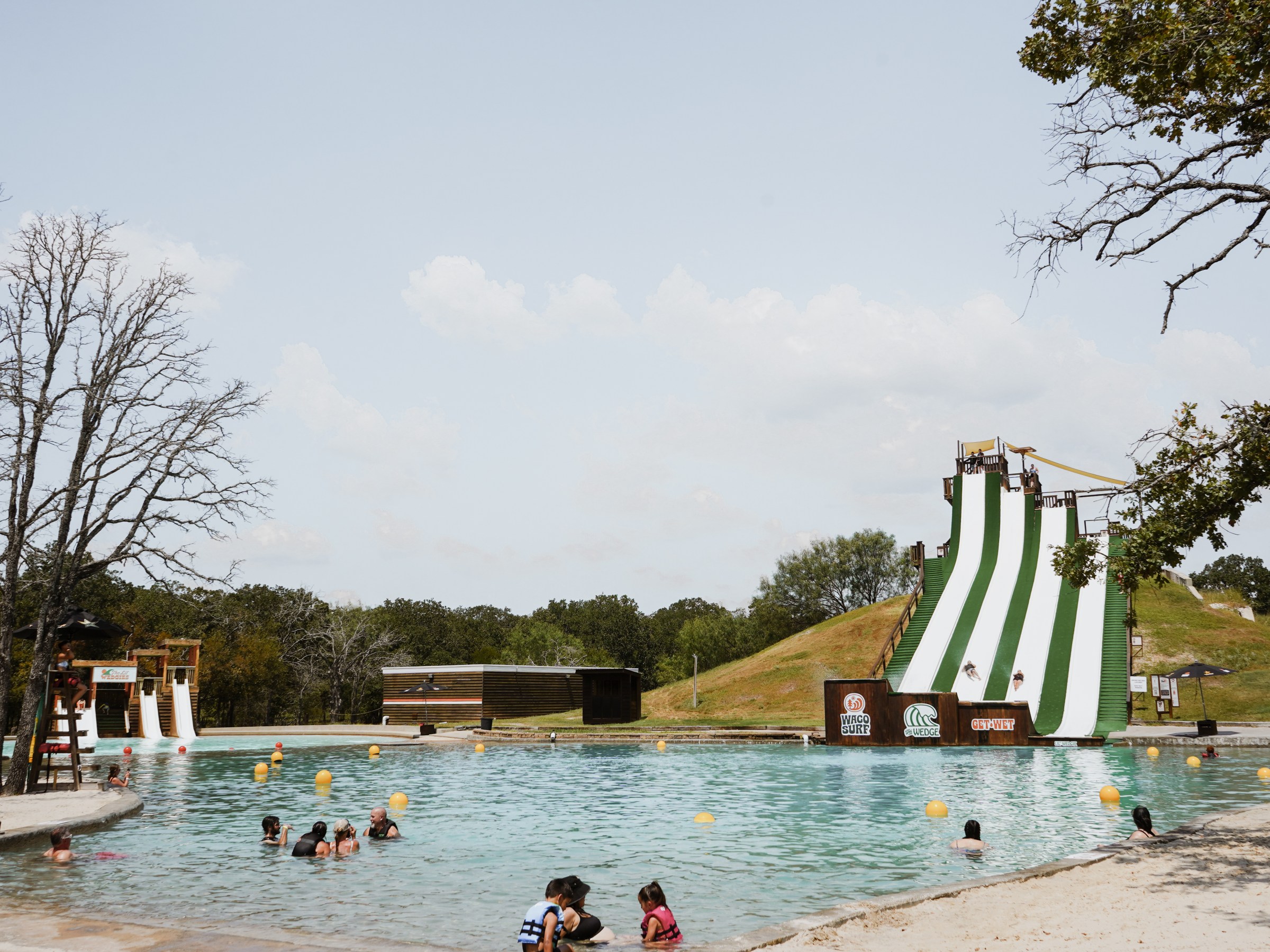 People swimming in a pool with large water slides and trees in the background.
