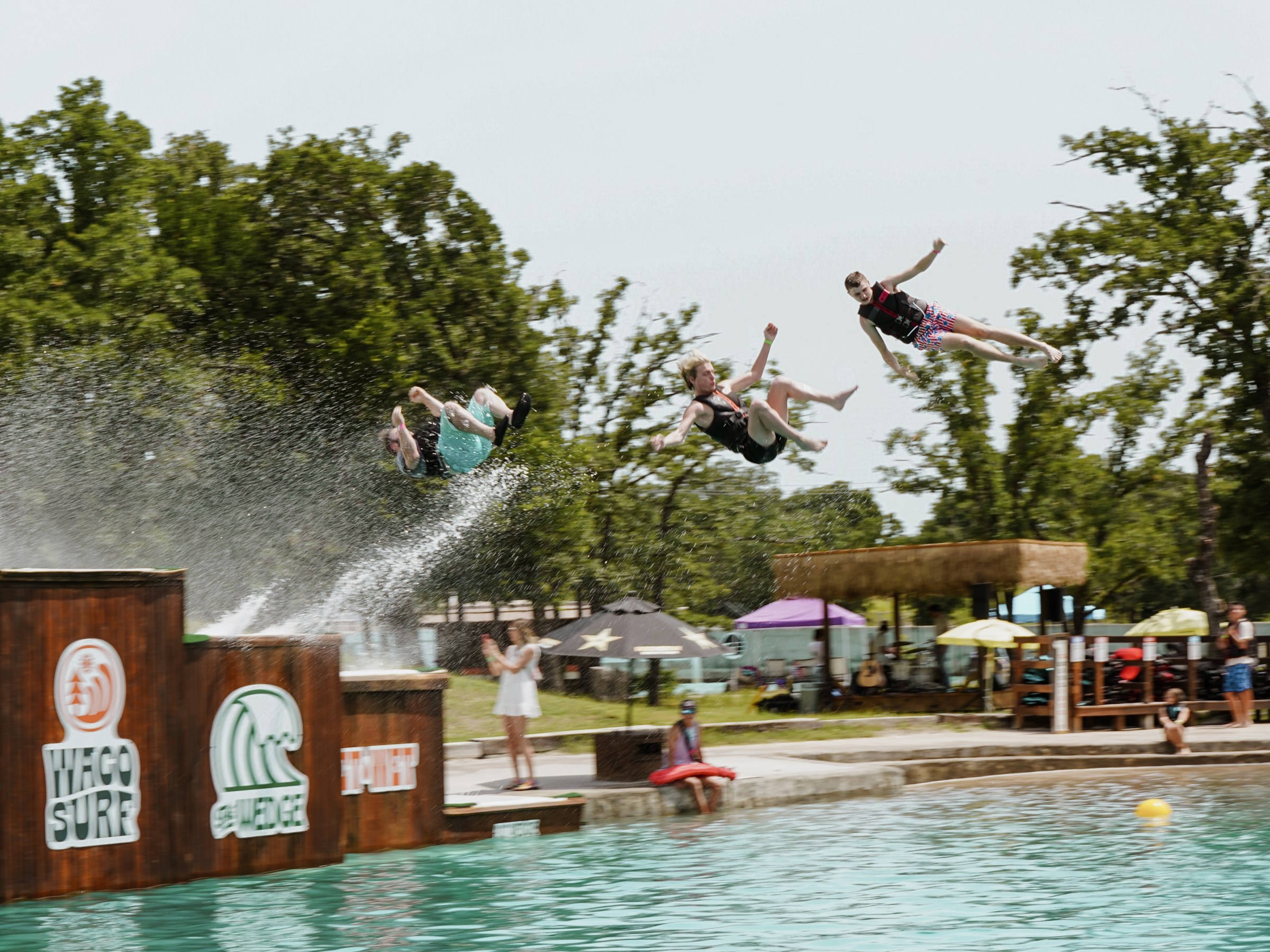 Four people mid-air jumping into a pool with trees in the background.